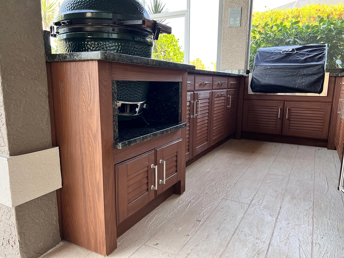 Outdoor kitchen with green egg grill, cabinets, countertop, and covering.
