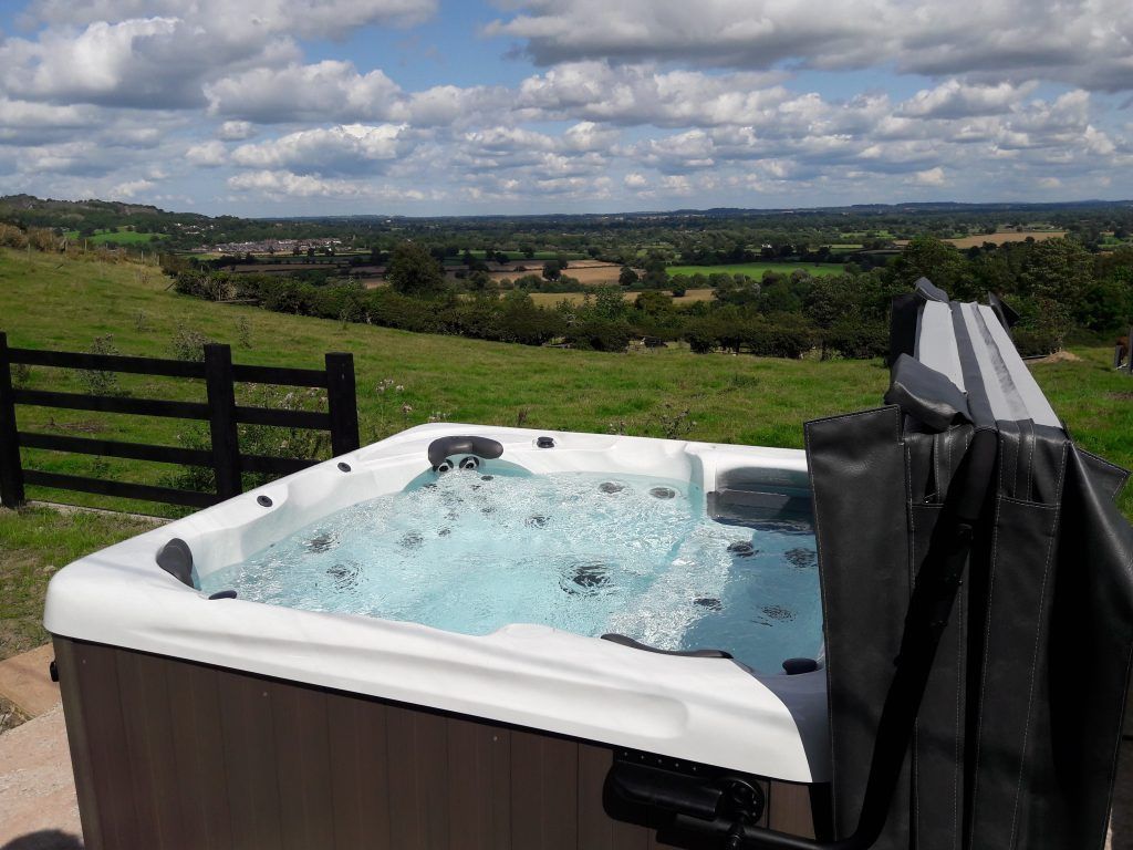 Hot tub outdoors with a scenic view of green fields and a blue sky with clouds.