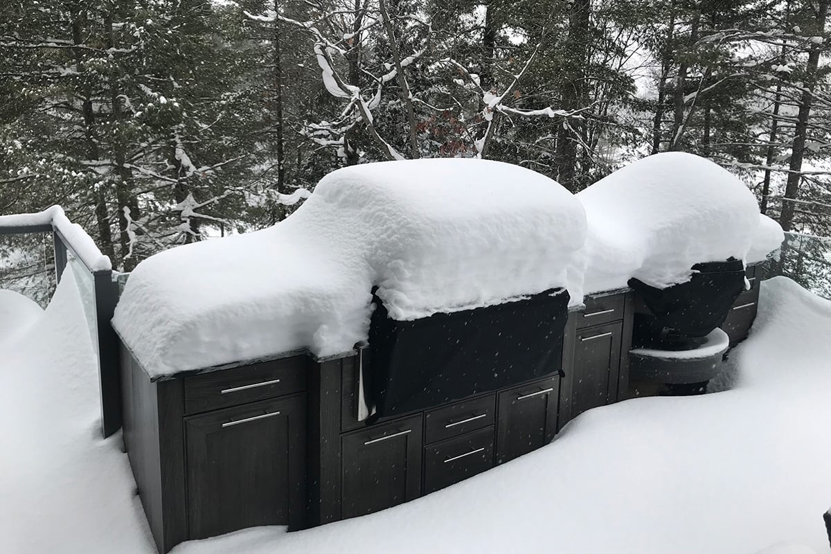Snow-covered outdoor kitchen on a deck, with trees in the snowy background.