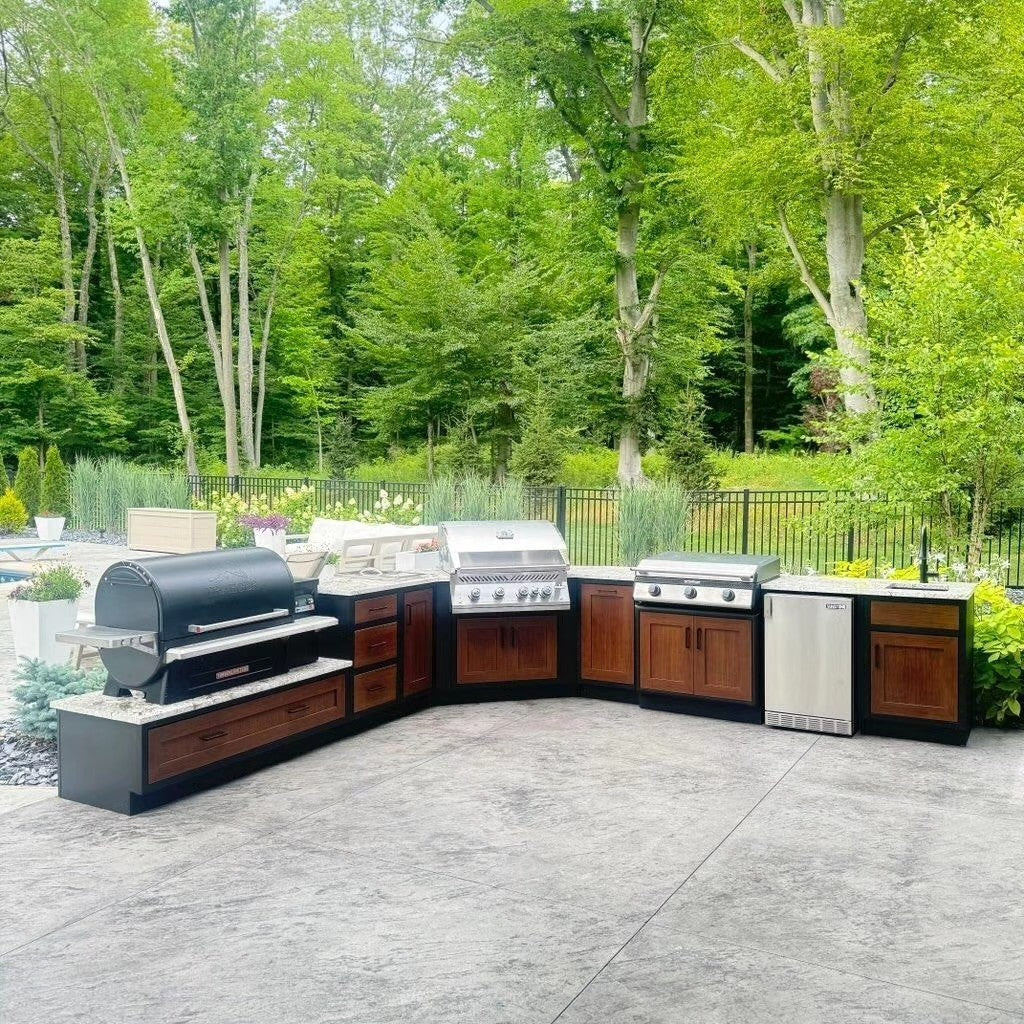 Outdoor kitchen with grill, cooktop, and refrigerator; surrounded by trees and greenery.