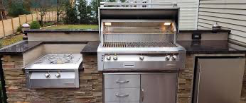 Outdoor kitchen with stainless steel grill, stovetop, refrigerator, and stone veneer facade.