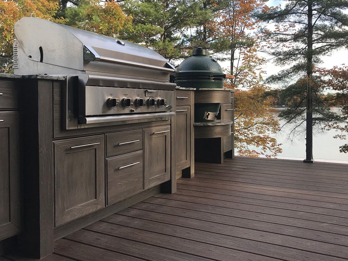 Outdoor kitchen with stainless steel grill and Big Green Egg overlooking a lake.