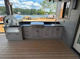Outdoor kitchen with gray cabinets, pizza oven, grill, sink, and water view.