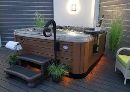 Hot tub on a wooden deck with steps, handrail, plants, and a small side table.