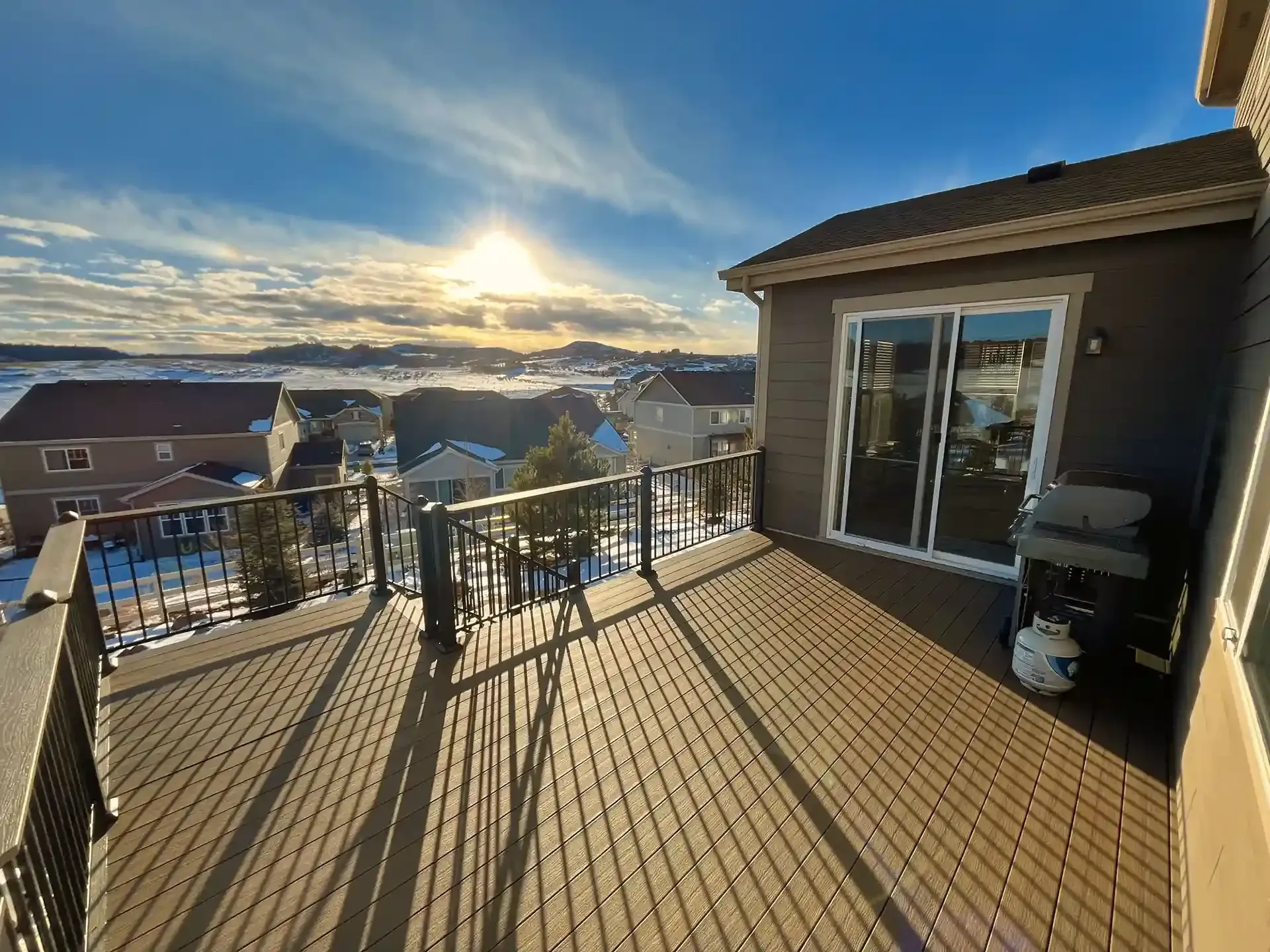 Wooden deck with mountain view, facing the sun, a house with sliding doors.