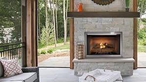 Fireplace with stone facade and wooden mantle in a room with a view of trees.
