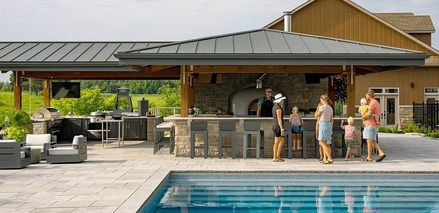 People near a backyard pool with a bar and outdoor kitchen.