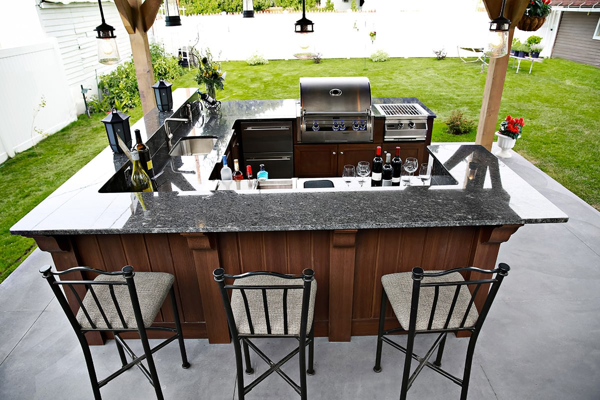 Outdoor kitchen with granite countertop, grill, bar seating, and green lawn.