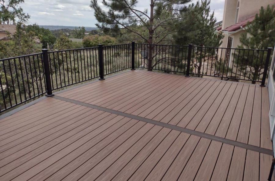 Wooden deck with black railing overlooking a green landscape.