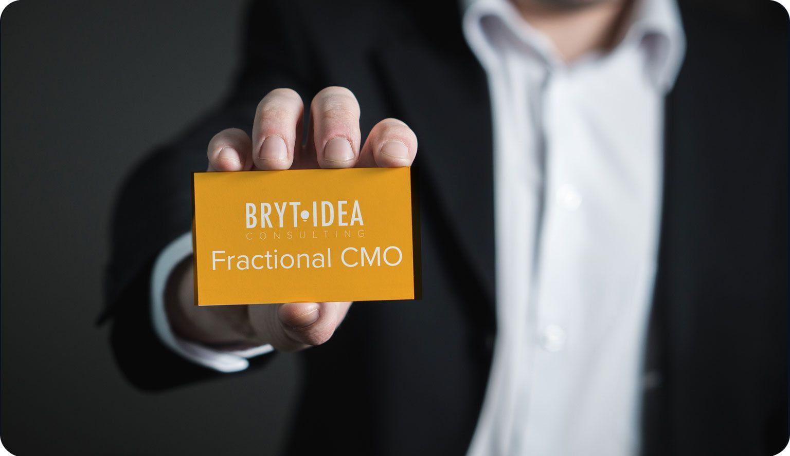 a man in a suit is holding a business card that says bryt idea consulting fractional cmo