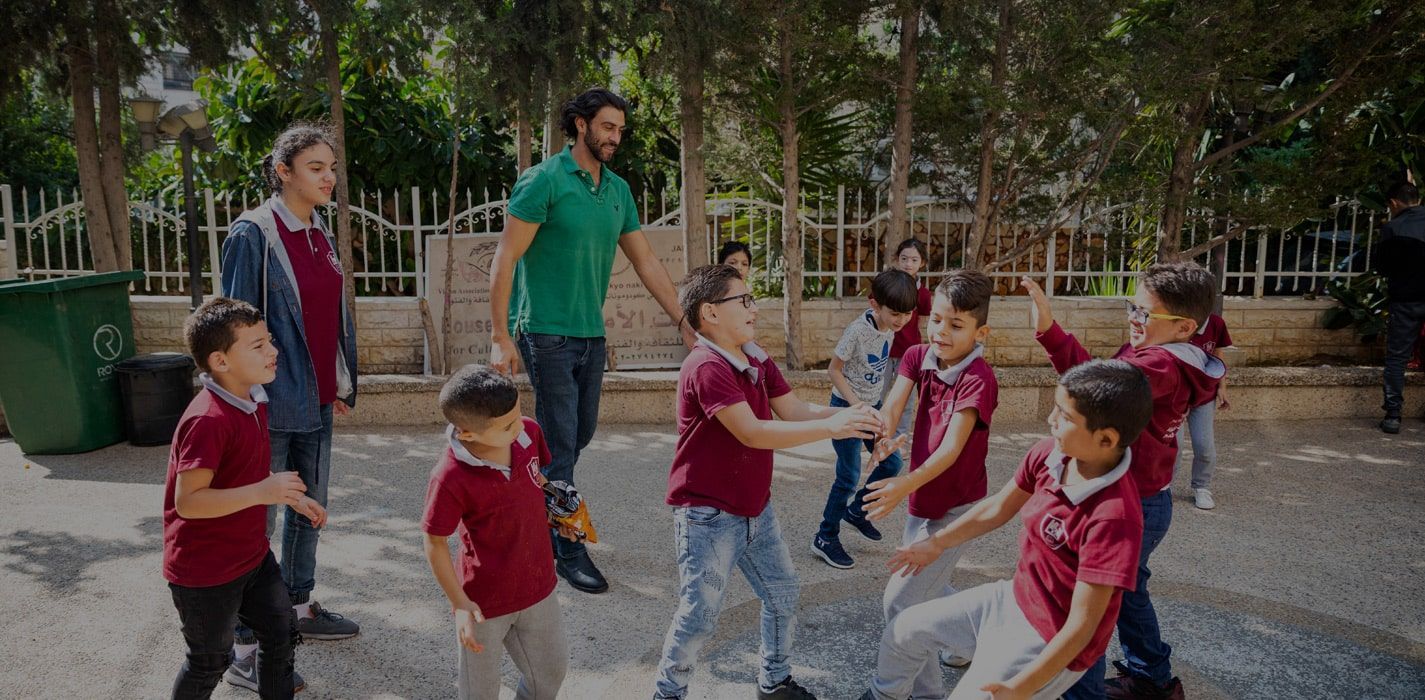 a group of children are playing with a man in a green shirt