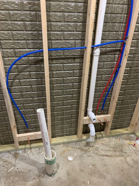 A bathroom with a brick wall and pipes coming out of it.