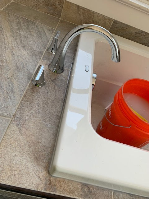 A bathroom sink with a bucket in it and a faucet.
