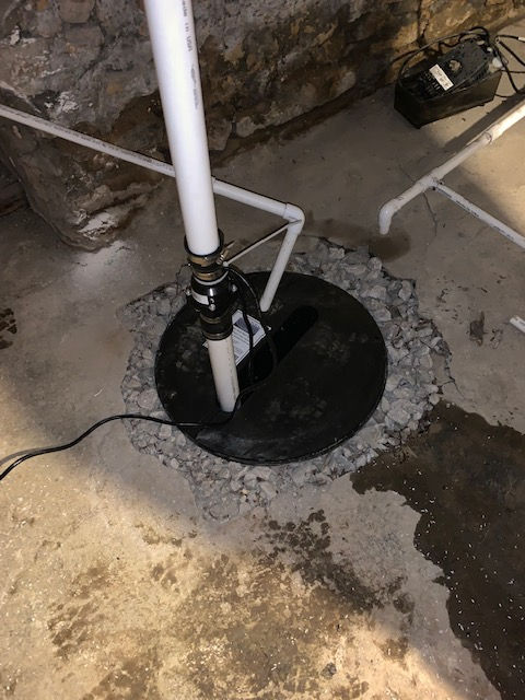 A sump pump is sitting on the ground in a basement.