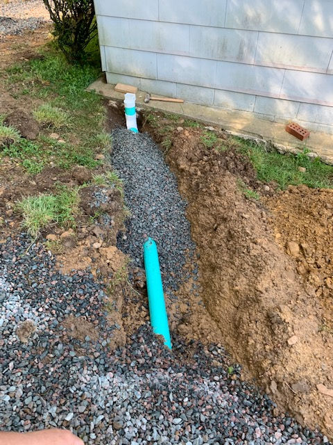 A green pipe is sitting in the dirt next to a house.