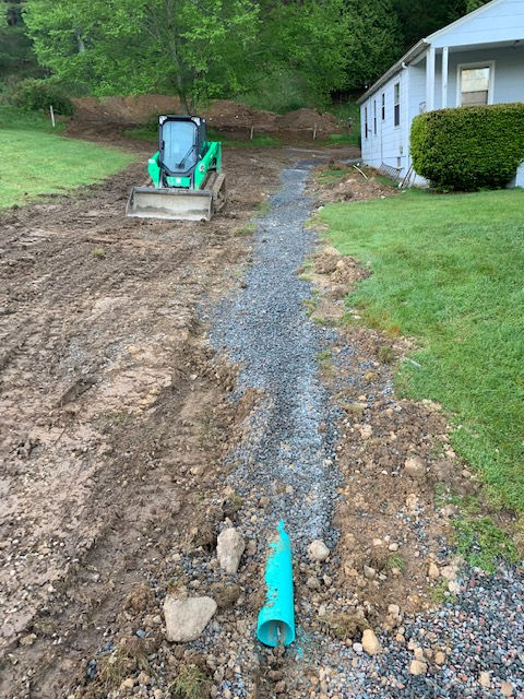A green tractor is driving down a dirt road next to a house.