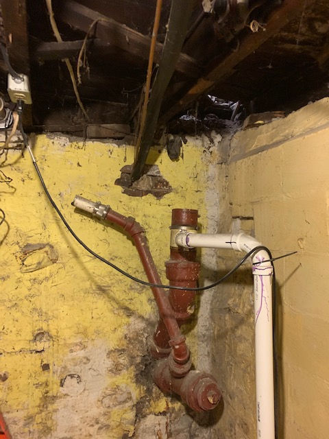 A red pipe is connected to a white pipe in a basement.