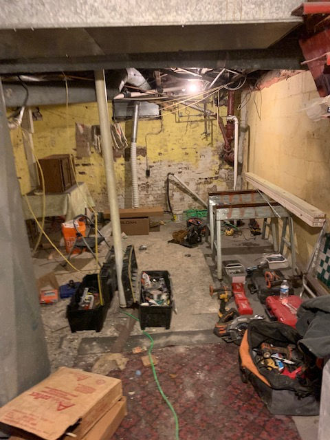 A messy basement with boxes and tools on the floor.