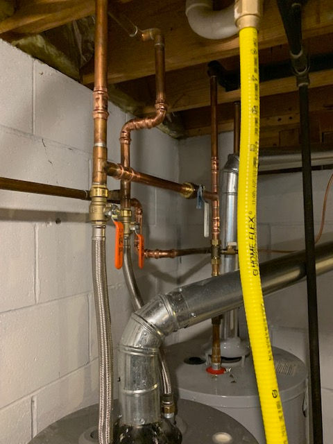 A yellow hose is attached to a water heater in a basement