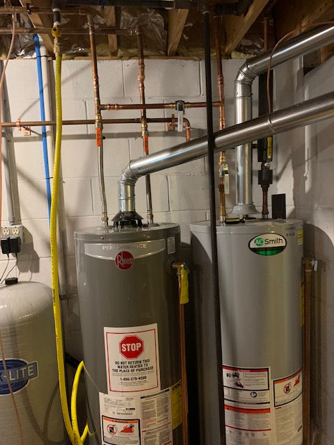 Two water heaters are sitting in a basement next to each other.