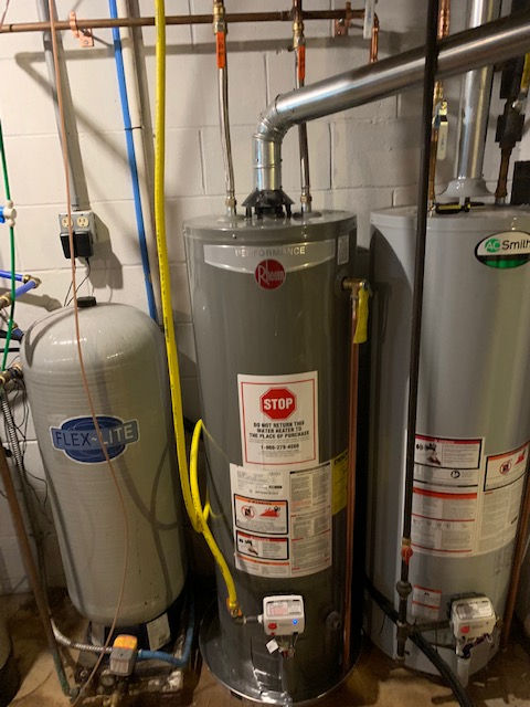 Two water heaters are sitting next to each other in a basement.