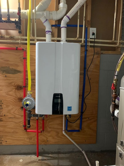 A white water heater is hanging on a wall in a basement.