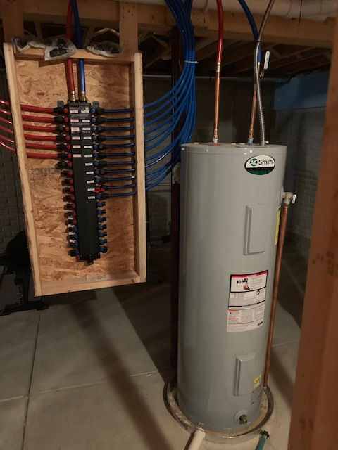 A water heater is sitting in a basement next to a electrical box.