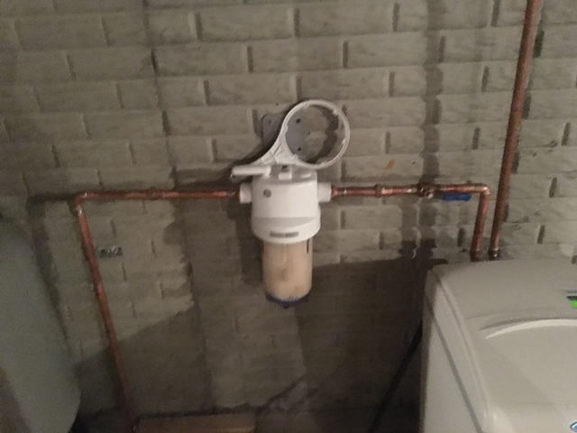 A water filter is attached to a copper pipe in a basement next to a washing machine.