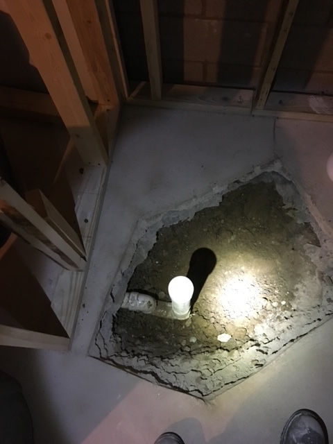 A person is standing in a hole in the floor with a flashlight.