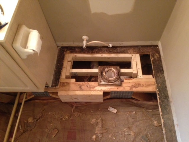 A toilet is being installed in a bathroom with a hole in the floor