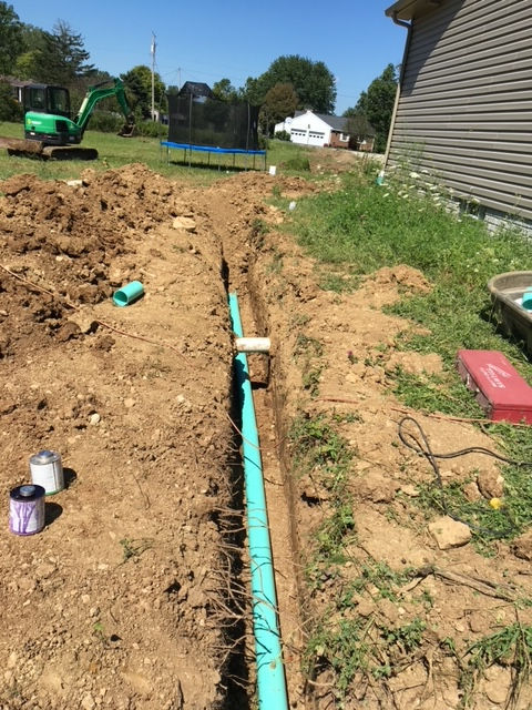 A green pipe is being installed in the dirt next to a house.