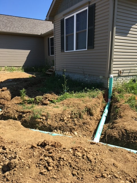 A house with a green pipe in the dirt in front of it