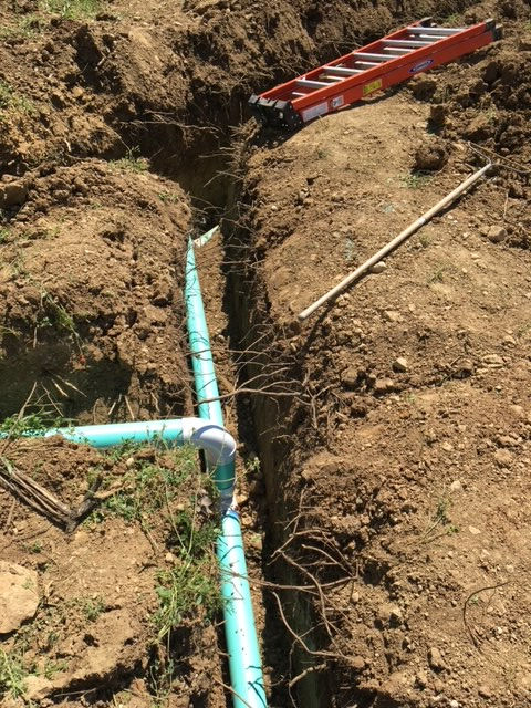 A ladder is sitting next to a pipe in the dirt.