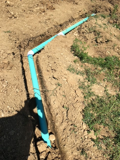 A blue pipe is laying in the dirt next to a grassy area