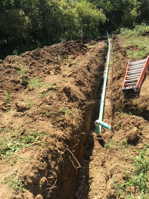 A ladder is sitting in the dirt next to a pipe in the ground.