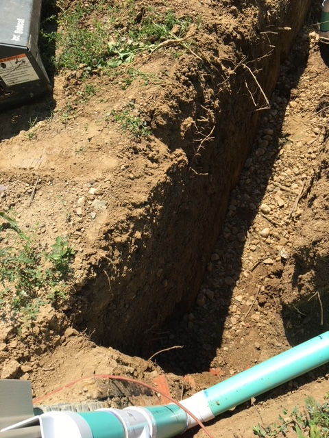 A green pipe is laying in the dirt next to a shovel