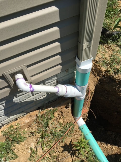 A green pipe is attached to the side of a house