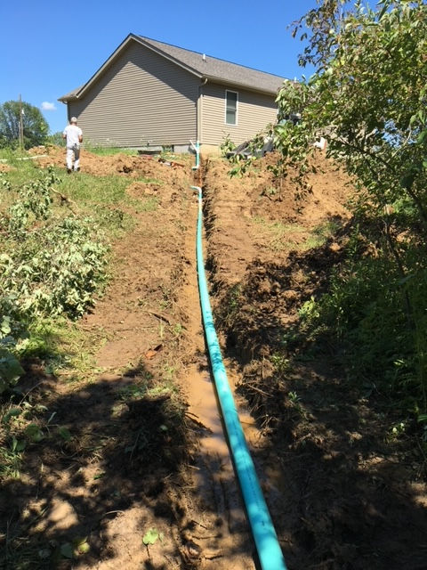 A green pipe is in the dirt in front of a house