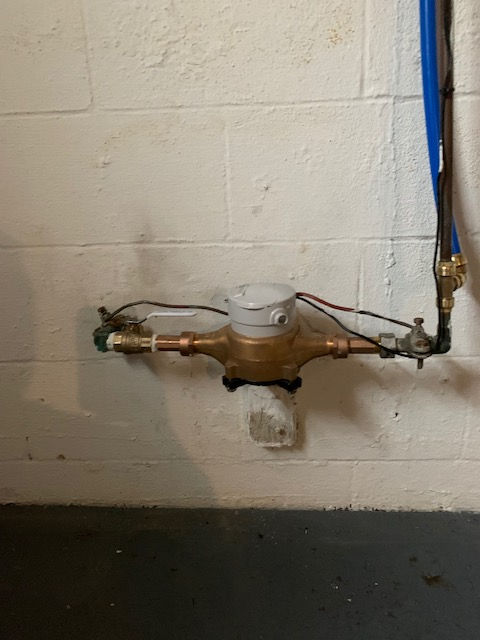 A water meter is attached to a white brick wall.