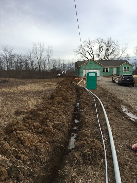 A green house is being built in the middle of a dirt field.