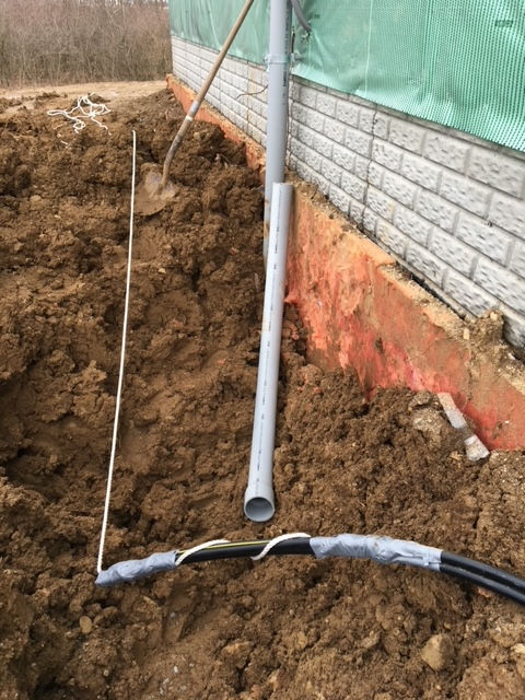 A pipe is laying in the dirt next to a brick wall