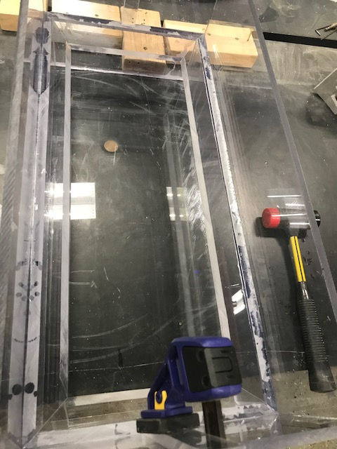 A hammer is sitting on a table next to a clear box.