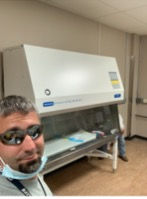 A man wearing a mask and sunglasses is taking a selfie in a lab.