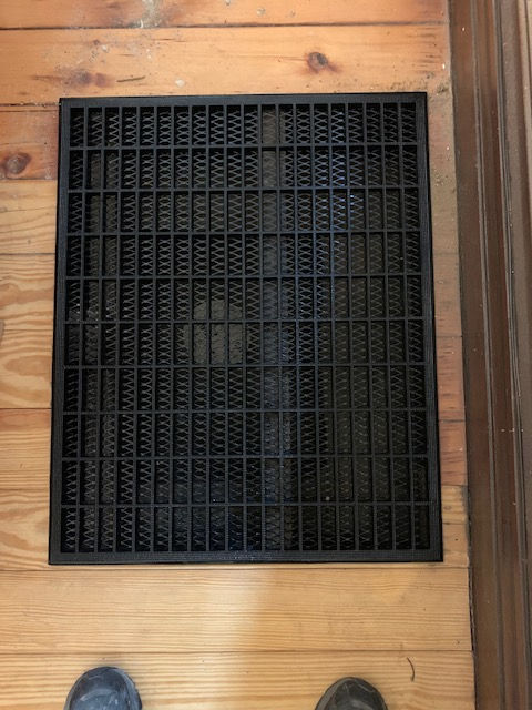 A person is standing next to a black mat on a wooden floor.