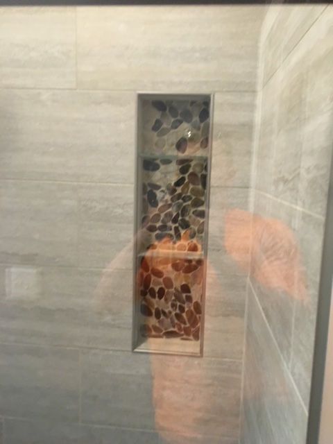 A person is standing in a shower with a shelf in the wall.