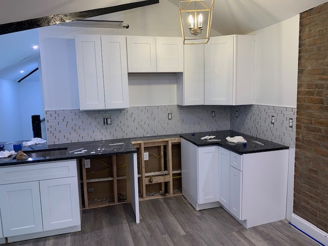 A kitchen under construction with white cabinets and black counter tops.