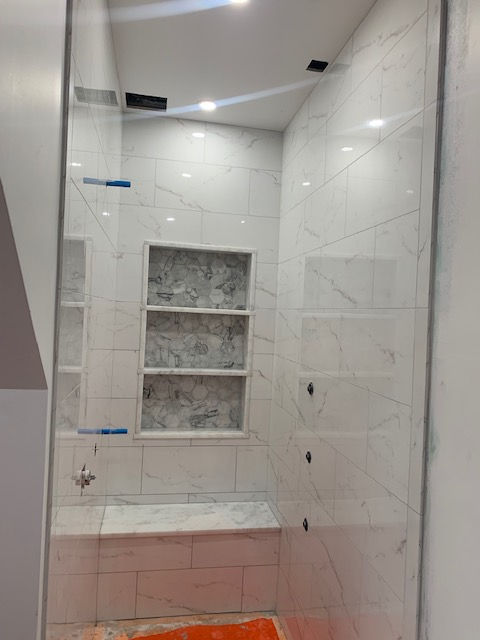 A bathroom with white tiles and a glass shower door.