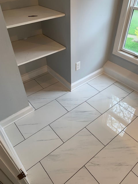 A room with white tile floors and shelves and a window.