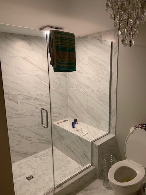 A bathroom with a toilet , shower , and chandelier.