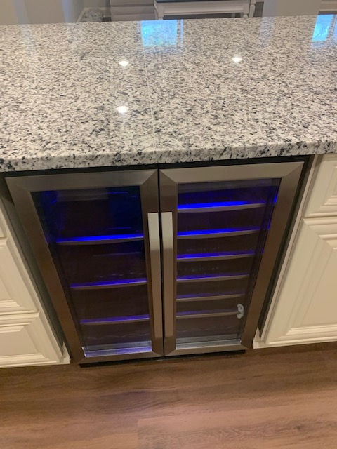 A wine cooler is sitting under a granite counter in a kitchen.